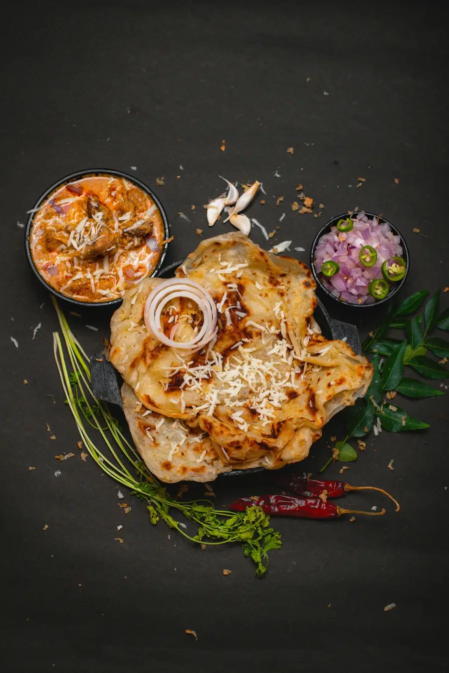Frisch gebackenes Naan auf dunklem Schiefer, daneben eine Curryschale, Zwiebeln und Chilischoten.