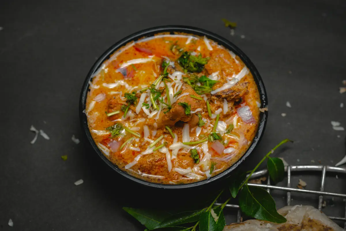 Cremiges Chicken Tikka Masala in einer schwarzen Schale auf dunklem Schiefer, mit Curryblättern.